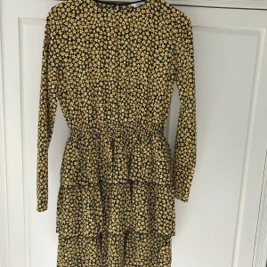 Envii klänning storlek XS - Gul och svart, blommig klänning från Envii. Aldrig använd, köpte inför en fest men hittade en annan klänning så den kom aldrig till användning.  Prislappen sitter kvar. Original pris 600kr. Resår i midjan, volanger i kjolen. Öppen (slits) i ryggen. Frakt tillkommer  