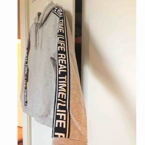  - Grå svinlen och mysig hoodie med text längs med armarna. Väldigt sparsamt använd. Frakt tillkommer!