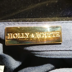 Holy and white hand bag  - Det är en mörk blå hand väska med rutigt mönster på gjort av polyester, den har även guld ditaljer på sig (inte äkta guld). Det är ett stort och öppet fack med en litet fack på sidan. Den är använd två gånger och har haft den ett år. Har använt den till shopping när jag inte har någon stans att lägga mina grejer, t.ex mobilen, plånbok mm.. Den skulle säkert vara fin till en svart klänning eller en basic outfit. 