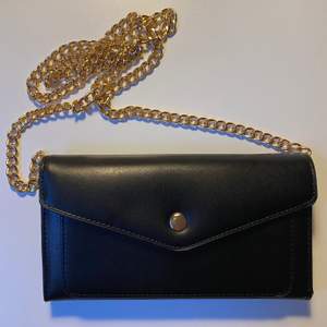 En svart handväska med borttagbar guldkedja