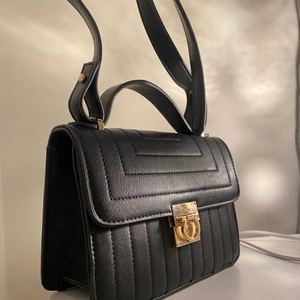 Svart Handväska med en liten guld detalj - Säljer min helt oanvända handväska köpt för 250kr i somras säljer för 100kr!! (KÖPAREN STÅR FÖR FRAKTEN)