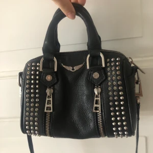 Zadig & Voltaire väska med nitar - Säljer min superfina Zadig väska med nitar för att jag tyvärr inte får användning för den längre, köptes i marbella för typ 3 år sedan. Fint skick inga märken eller så och dustbag medföljer! Frakt tillkommer. Buda från 1500