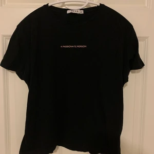 Croppad t-shirt från NA-KD, storlek XS - Svart croppad t-shirt från NA-KD i storlek XS, med ljusrosa tryck (”A passionate person”). Tröjan är ganska använd, men ändå i bra skick. Trycket har fadeat litegranna, men det är inget man märker om man inte kollar noggrant. Köparen står för frakten!