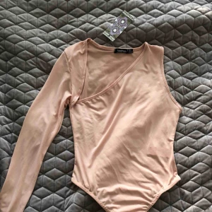  - En ljusrosa body med en arm, helt oanvänd och prislapp kvar.