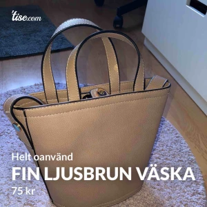  - En fin brun väska som är oanvänd och helt ny! Den är rund i botten, har ett stort fack och sedan två små inuti! Stängs med en knapp längst upp, har både handtag och axelrems band! 