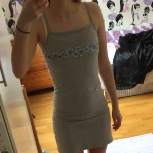  - Grå mjukisklänning med blå blommor på bröstet. Perfekt både till finare tillställningar men även till vardag 