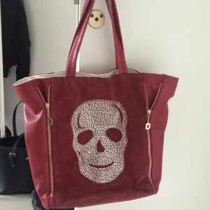  - Vinröd rymlig väska med broderad döskalle av små "diamanter". Mocka imitation på framsidan och resten i konstläder. Vitt innertygg