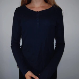  - En mörkblå tröja med knappar. 