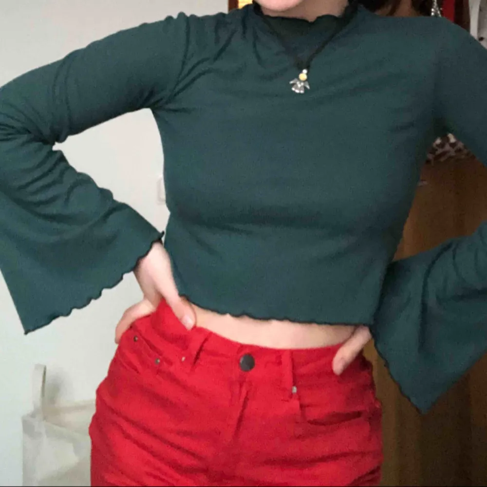 En grön halvpolo typ med frans/volang från nakd. Den har trumpetärmar och är cropped (slutar där högmidjade jeans oftast slutar). Knappt använd alls då den inte riktigt är min stil🥰 passar nog xs och s. Toppar.