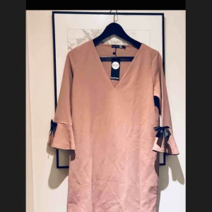  - Oanvänd! Långärmad klänning i fin rosa färg. Säljer då den inte riktigt är min stil. Rosetterna går lätt att sprätta bort om man skulle vilja det. Skickas mot frakt eller upphämtning i Bergshamra.