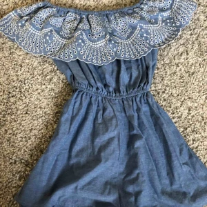  - Blå off shoulder jumpsuit med mönstrad spets fram. Storlek 36, aldrig använd!