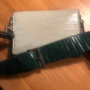  - Grön och mintfärgad väska från Carin Wester  Fint skick! Ingår även ett smalt axelband till (oanvänt) se bild nr 3.     