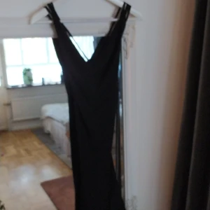 Svart figursydd klänning i stretchigt material - Urringad med jätteläcker snörning i ryggen och assymetrisk nertill. Strl S, passar även M 
