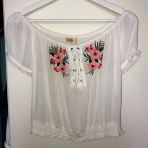 Vit blus - En super fin vit blus med en liten knytning och två blommor, tyvärr för liten för mig! Kan användas som både offshoulder och vanligt💕 Inte så genomskinlig som den ser ut!! Använt endast 3 ggr. Frakt tillkommer!💗