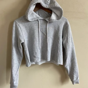 Midje Hoodie  - Midje-lång hoodie från Bikbok, extra mysigt tyg inuti. Med huva & med ”rå” kant (den ser ut att vara som avklippt i nederkanten). Säljer då den aldrig används. I storlek S och nytt skick. 
