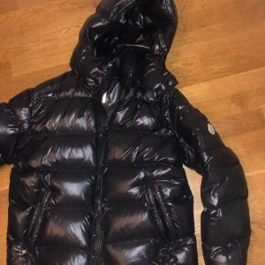 Moncler Maya Size 4 -  Moncler jacka herrmodell Maya i svart färg. Endast använd en vinter så den är i väldigt fint skick. Köpt på sensse för 10 500 SEK förra vintern. Tags följer med, kvitto finns digitalt.