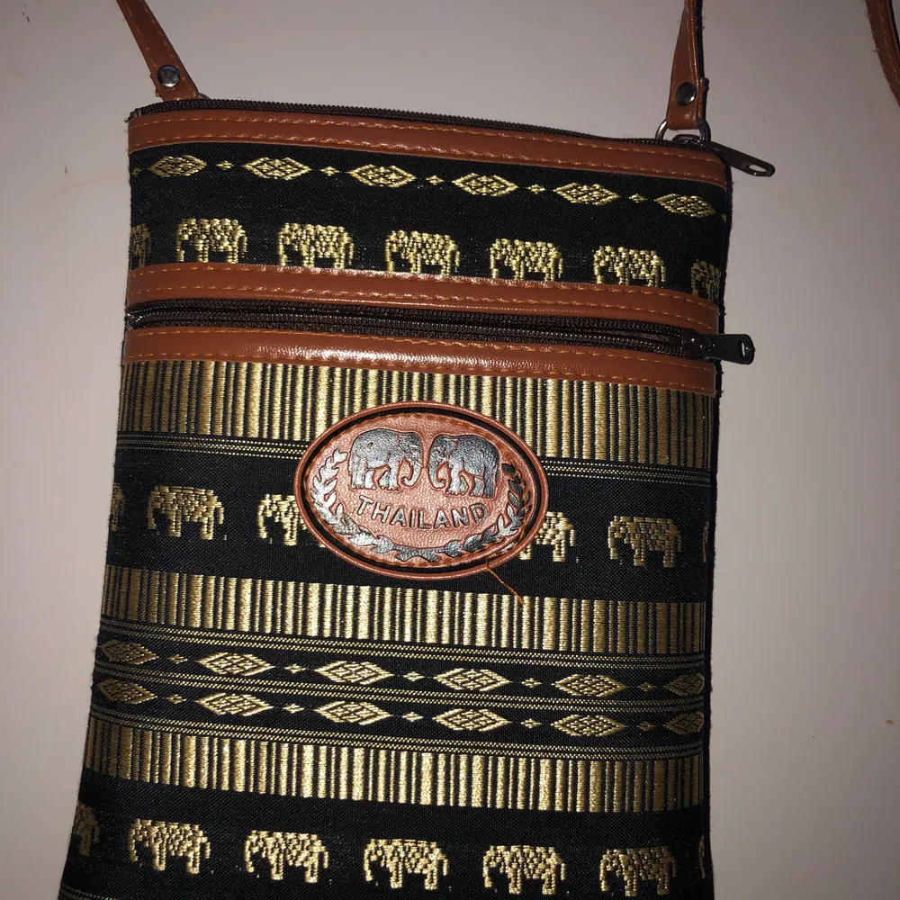 Så cool väska som är köpt i Thailand och helt unik. 2 st fack, praktisk. Guldiga elefanter och mönster. Brunt axelband. Köpt för 199 kr säljer för 40 kr.. Väskor.