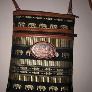 Så cool väska som är köpt i Thailand och helt unik. 2 st fack, praktisk. Guldiga elefanter och mönster. Brunt axelband. Köpt för 199 kr säljer för 40 kr.
