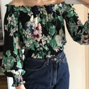 Blommig tröja strl S - Somrig off-shouldertopp i stretchigt material med "lettuce-hem". Lite croppad i modellen och använd men i fint skick. Dock har en av resårtrådarna i mudden lossnat lite, kan skicka en närmare bild vid intresse. Köparen står för frakt!🌻