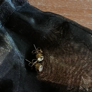 DYRBERG/KERN  - Enkla stilfulla örhängen med en polerad guldtonad yta och en vit patienskristall från Swarovski. 