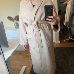 Zara Ullkappa - Beige - Jättefin beige/sandfärgad, lång kappa från Zara med bälte i midjan som ger en fin siluett! Innehåller 44% ull. Är i storleken S, men är lite oversized så skulle säga att den passar allt från S-L beroende på hur man vill att den ska sitta. Köparen står för frakten 🧚🏼‍♂️