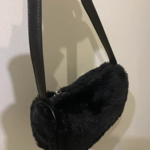 Axelväska - Liten fin Axelväska i mycket bra skick, använd under 5 gånger, köpt på Nelly. Mjukt fluffigt material i färgen svart. Mitt pris 60kr