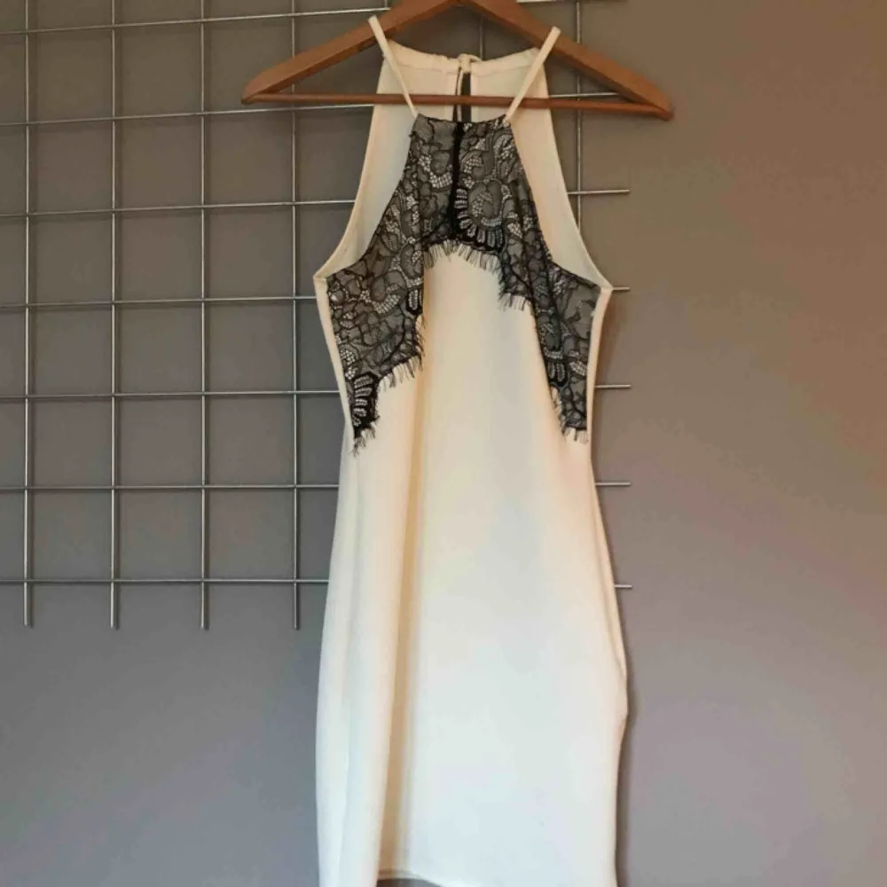 Kort vit klänning i halterneck-liknande modell med svart spets framtill. Endast använd 1 gång. Passar storlek XS/S.. Klänningar.