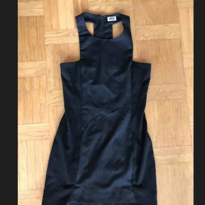  - Svart kort tight klänning från Weekday. Kortare framtill och olika typer av tyg i sidorna mot rygg och framtill. Dold dragkedja i ryggen. 