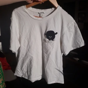 T-shirt  - Vit t-shirt med en liten lurvig filur på som flyger ut ur en ficka. Från Monki. Lite croppad. Väl andvänd