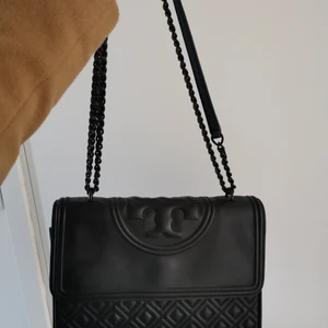 Tory burch väska - Väska i mattsvart läder. Ca ett år gammal men i fint skick utanpå och innanpå. Något nött på knappkanten under locket men inget som syns/stör. 