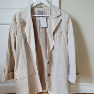 Beige linnekavaj  - Oanvänd linnekavaj i ljus beige färg. Har axelvaddar som markerar axlarna och är väldigt oversize!
