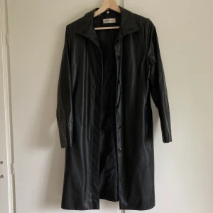 Skinnrock storlek 38 - Supersnygg lång svart skinnrock/kappa. Storlek 38. Den perfekta jackan nu i höst, så cool! I fuskskinn.