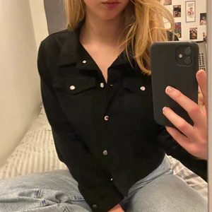  Jacka svart strl M - Jackan är i mockaimitation med silvriga detaljer. Den är kort och slutat lite under midjan. Jackan har även två fickor vid bröstet på vars sin sida. Den är tunn i tyget och funkar som en sommarjacka. Köparen står för frakten (48kr)