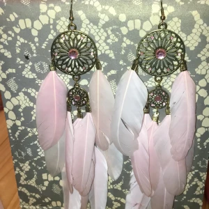 Festliga fjäderörhängen  - Fina örhängen för fina tillställningar med alla rosa stenar kvar samt alla rosa fjädrar. Fjädrar är såklart ömtåliga och har levnadstecken, därför de är billigare. Säljes för att jag inte inte använder dem.