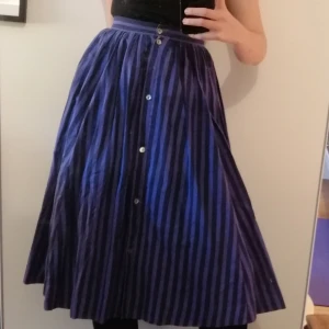 Lila bomullskjol - Fin randig lila bomullskjol, knäpps med knappar framtill och baktill. Skulle gissa storlek xs-s. Har fickor, så skön och praktisk! Riktigt bra kvalitet, har fått ärva den av min farmor som haft den i många år. Frakt tillkommer 