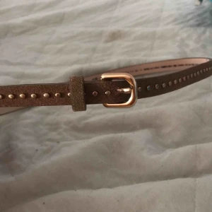  - Två skärp  1 brunt med guldnitar och guldspänne har endast 1 hål men kan göra fler 1 vitt flätat med guld spänne passar alla då de har hål överallt  20kr styck båda för 30kr