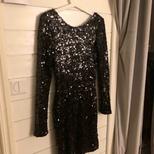  - En svart glittrig klänning från Nelly.com. ANVÄND 1 GÅNG! Klänningen slutar ungefär under knäna för mig som är 168cm. Klänningen har svarta lite större paljetter och har en djup rygg där bak. Passar väldigt bra till fest/nyår!