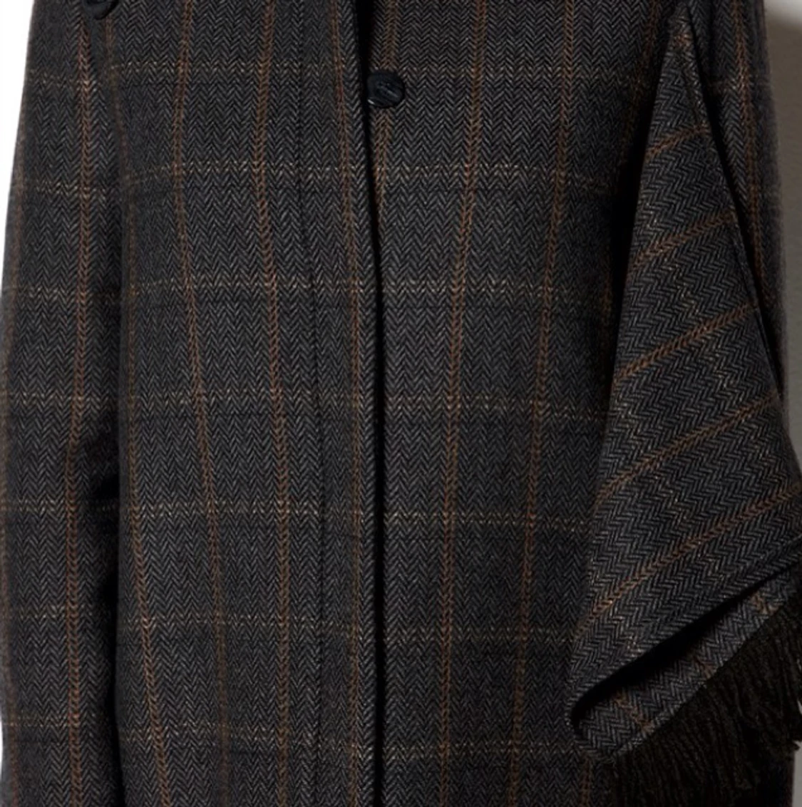 Rodebjer Connor 
Varm och stilig yllekappa i tweed från Rodebjer. Kappan har dold knäppning fram samt två fickor. Baktill finns ett långt sprund med dolda knappar och ett tygstycke med fransar går från baksidan och knäpps fram över livet - 1378449022