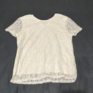Vit spetsblus från Hailys - Supersöt vit blus från Hailys i transparent spets med blommigt mönster. Kortärmad modell med rund halsringning och fina spetsdetaljer längs kanterna. Perfekt för dig som gillar romantisk och feminin stil.