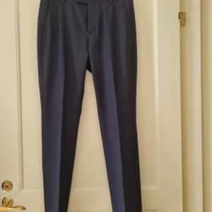 Mörkblå kostymbyxor från H&M strl 46 - Snygga mörkblå kostymbyxor från H&M i slim fit. Perfekta för en skolavslutning. Byxorna har en klassisk design med knappar bak och dragkedja fram. Storlek 46. Kan hämtas i Vallentuna.