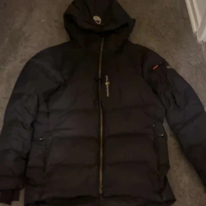 Svart pufferjacka Sail Antarctica - Sail racing jacka, ok skick några skador men väldigt små dock! Ganska chuncky och stor I storlekan så rekommenderar den här för storlek M