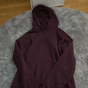 Mörklila hoodie från Gina Tricot - En stilren mörklila hoodie från Gina Tricot med huva och känguruficka framtill. Tröjan har långa ärmar och är tillverkad i mjuk bomullsmix, perfekt för mysiga dagar. Enkel och snygg design som passar till det mesta.