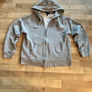 Ralph Lauren - Grå Polo Ralph Lauren zip-hoodie Superfin luvtröja i mjukt material – perfekt för vintern! Storlek på lappen: XL (18–20), men passar mer som S–M. Väldigt fin färgkombination och klassisk Polo-logo. Längd: ca 50 cm Axel till axel: ca 40 cm  💬 Fråga gärna om du vill ha fler bilder eller mått!  ⚡ VIKTIGT: Köp fler än 1 plagg så får du rabat – värt det och bra för kortet 🤗😂  #ralphlauren #polo #hoodie #luvtröja #ziphoodie #grå #streetwear