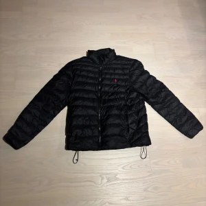 Svart dunjacka från Polo Ralph Lauren - Svart dunjacka från Polo Ralph Lauren med röd logga på bröstet. Köpt på NK med vädligt bra skick. Priset kan sänkas! Skriv om du har fler frågor 😁den är storlek L