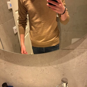 Beige merinoulls tröja från J.Lindeberg - Snygg beige stickad tröja i merinoull från J.Lindeberg med diskret JL-logo på bröstet. Använd max 5 gånger så den är i topp skick! Tröjan har rund hals och långa ärmar, perfekt för dig som gillar stilrena och enkla plagg. Materialet är mjukt och skönt, passar till många olika looks.