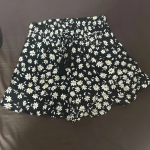 Svarta shorts med blommor - Svarta shorts med vita blommor. De har en bekväm elastisk resår och snörning framtill