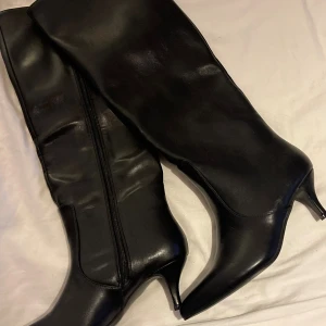 Svarta stövlar med klack och spetsig tå - Snygga svarta stövlar i skinn med spetsig tå och smal klack. Stövlarna har dragkedja på insidan och en elegant, tidlös design som passar till många outfits. Perfekta för dig som vill ha en klassisk och stilren look.