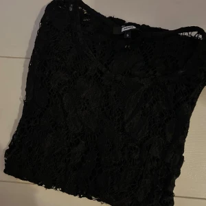 Svart spetsblus från Bik Bok - Svart blus från Bik Bok i genombruten spets med blommigt mönster. Blusen har rund halsringning och är ärmlös, perfekt för att skapa en cool och trendig look. Materialet är lätt och luftigt, vilket gör den enkel att styla över ett linne eller bralette. Perfekt att ha över ett linne eller fest tröja. Pris 60kr och storlek s. 