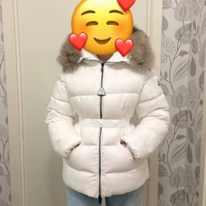 Moncler dunjacka med äkta päls - Säljer en snygg vit Moncler dunjacka med fluffig äkta päls. Jackan har avtagbar bälte i midjan, dragkedja framtill och Moncler-logga på ärmen. Perfekt för kalla vinterdagar och har en riktigt lyxig vibe. Jackan är endast testad på! 