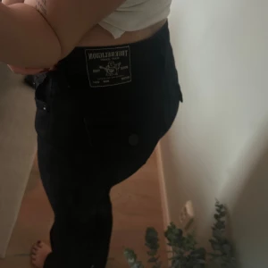 Svarta jeans från True Religion - Säljer ett par svarta jeans från True Religion med ikonisk bakficka och tydlig logopatch i midjan. Jeansen har en snygg, rak passform och är tillverkade i ett slitstarkt jeansmaterial. Perfekt för dig som gillar streetstyle och vill ha ett par jeans med coola detaljer.